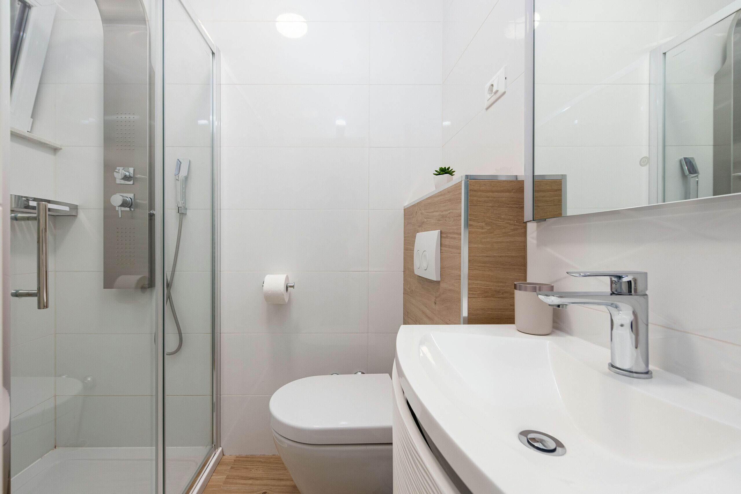 A modern bathroom with a glass-enclosed shower, a white toilet, and a sink with a mirror.