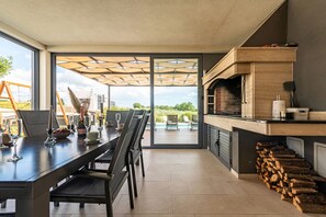 Eine moderne Küche mit einem großen Esstisch, einem eingebauten Grill und Blick ins Freie.
