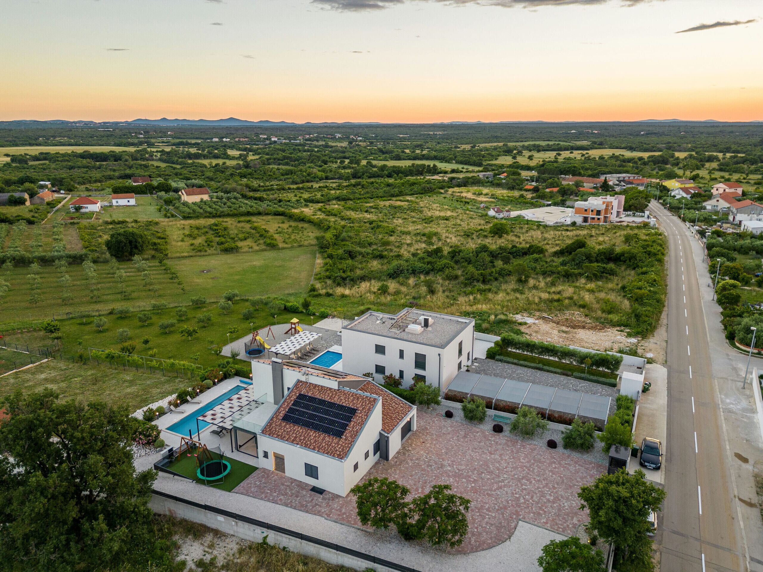 A modern building with a swimming pool, solar panels, and a paved driveway.