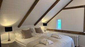 A bedroom with a sloped ceiling, white bedding, two bedside lamps, a window, and a radiator. - Aðalstræti - Historic Luxury Villa (Akureyri)