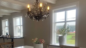 A dining area with a white table, wooden chairs, a chandelier, and a view of the outdoors through large windows. - Aðalstræti - Historic Luxury Villa (Akureyri)