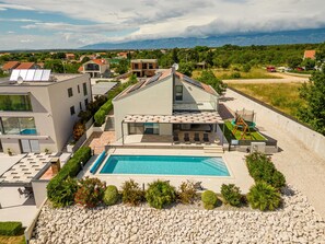 Ein modernes Haus mit Swimmingpool, umgeben von einem angelegten Garten und Blick auf die Berge.