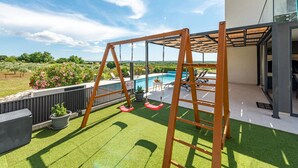 A patio with artificial grass, a swing set, a pool, and a modern building with glass doors. - Villa Descansa Zadarvillas (Nin)