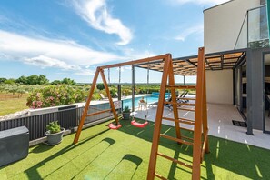Eine Terrasse mit Kunstgrasanlage, einer Schaukel, einem Pool und einem modernen Gebäude mit Glastüren.