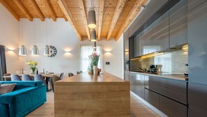 A modern kitchen with a central island, wooden ceiling beams, pendant lighting, and a dining area with a teal sofa. - Villa Descansa Zadarvillas (Nin)