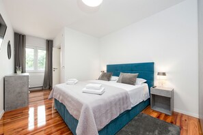 Ein modernes Schlafzimmer mit einem großen Bett, einem Nachttisch mit Lampe und Blick ins Freie durch ein Fenster.