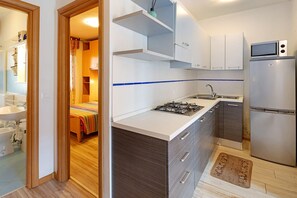 A compact kitchen with a gas stove, a microwave, and a refrigerator. - Villa 'Antares Trilocale' with Private Terrace, Garden, and Air Conditioning (Bibione)