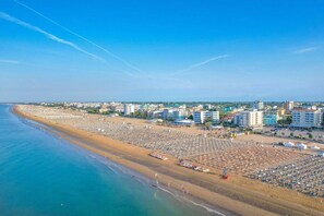 A coastal cityscape with a wide beach, numerous beach umbrellas, and buildings along the shoreline. - Villa 'Antares Trilocale' with Private Terrace, Garden, and Air Conditioning (Bibione)