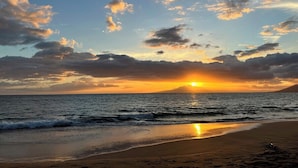 A beach with the sun setting over the ocean, creating a silhouette of a distant landmass. - 2BR ¼ mi to Kam 1 Beach, Pool, Hot Tub, Gym, BBQ (Kihei)