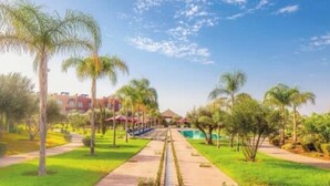 Un sendero lleva a un edificio con piscina, rodeado de palmeras y follaje.