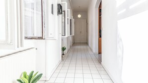 Un couloir étroit aux murs et au sol recouverts de carreaux blancs, qui mène à une porte au fond.