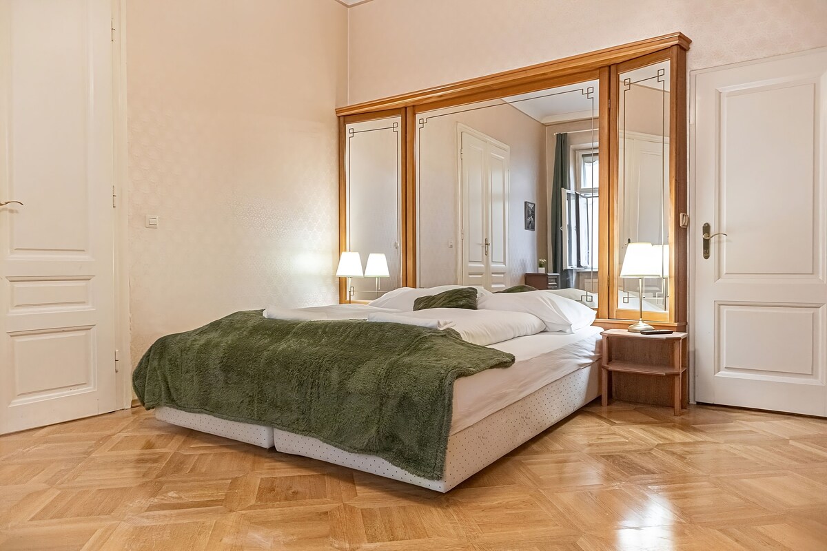 A bedroom with a bed, two bedside lamps, a mirror, and a wooden floor.