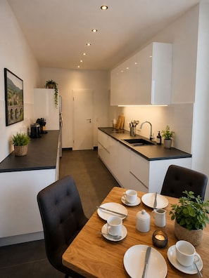Een moderne keuken met witte kasten, een zwart aanrecht en een eethoek met een houten tafel voor twee personen.