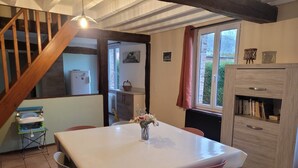 A dining area with a white table, red chairs, a vase with flowers, a wooden cabinet, and a staircase. - Bridge meadows (Grainville-la-Teinturière)