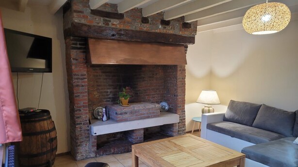 A cozy living room with a brick fireplace, a sofa, a coffee table, and a television mounted on the wall. - Bridge meadows (Grainville-la-Teinturière)