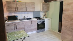 A compact kitchen with wooden cabinets, a microwave, a gas stove, and a small sink. - Bridge meadows (Grainville-la-Teinturière)