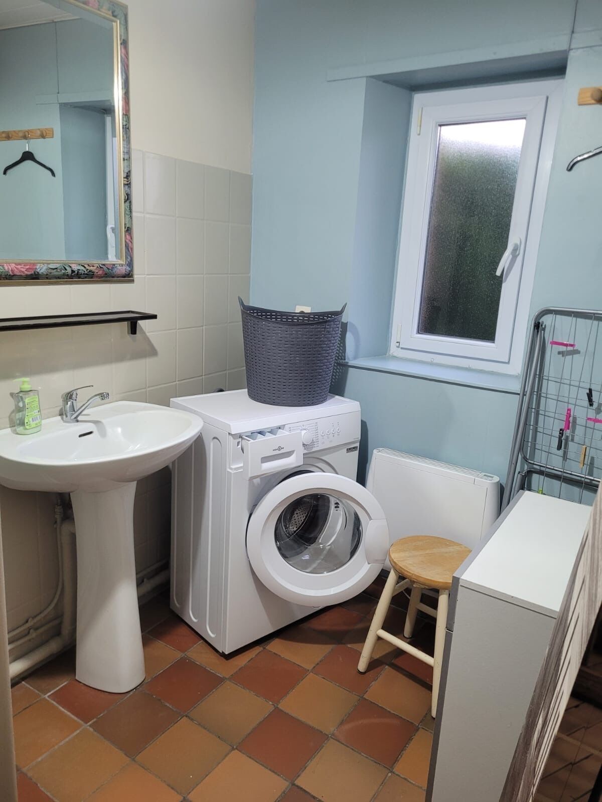 Ein kleines Badezimmer mit Waschbecken, Waschmaschine und einem kleinen Hocker.