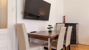 A dining area with a wooden table, four chairs, a television mounted on the wall, a small potted plant, and a decorative item on a cabinet. - Spacious 2BR Apartment Long Stay Vienna (Vienna)