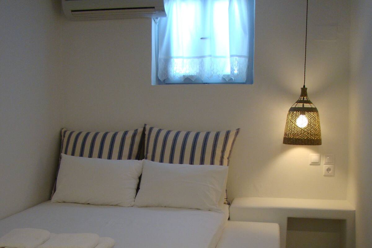 Una cama bien hecha con ropa de cama a rayas, una mesita de noche con lámpara y una ventana con cortinas.