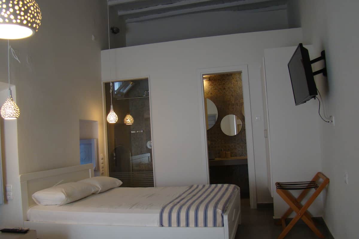 Un dormitorio con cama, mesita de noche, lámpara y televisor instalado en la pared.
