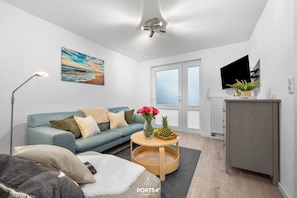 A modern living room with a sofa, a coffee table with flowers, a TV, and a cabinet. - Kleene Buud - cozy apartment on the ground floor, 2 persons, quiet and central location (Büsum)