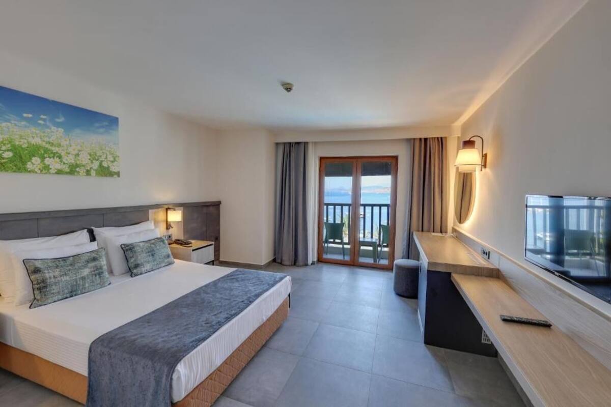 Ein Hotelzimmer mit Bett, Schreibtisch, Fernseher und einem Balkon mit Vorhängen.