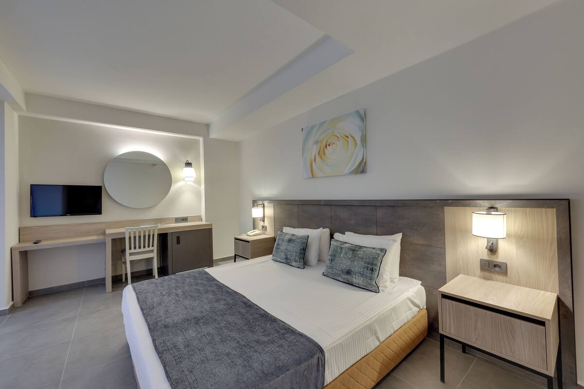 Ein modernes Hotelzimmer mit einem großen Bett, einem Schreibtisch, einem Sessel und einem Fernseher.