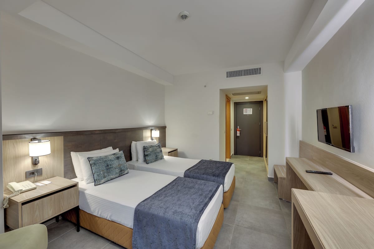 Une chambre d’hôtel avec deux lits, un bureau, une chaise, une télévision et un téléphone.