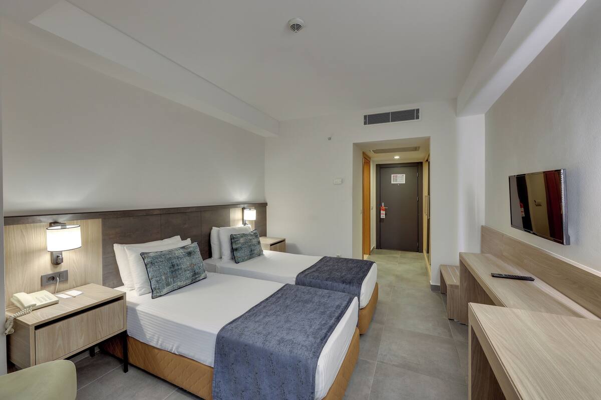 Ein Hotelzimmer mit zwei Betten, einem Schreibtisch, einem Stuhl, einem Fernseher und einem Telefon.