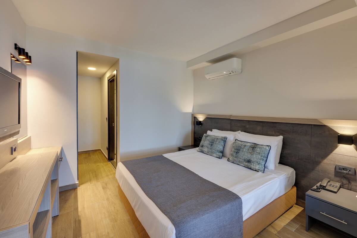 Ein modernes Hotelzimmer mit einem großen Bett, Nachttischen, einem Schreibtisch und einem Fernseher.
