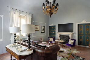 Ein Wohnzimmer mit einer Chandelier, einem Kamin, einem Fernseher und einem Ledersofa.