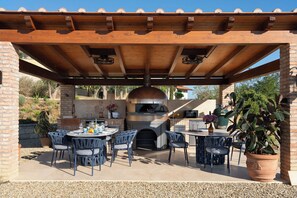 Une terrasse extérieure dotée d’un four en briques, de sièges et d’une structure en forme de pergola.