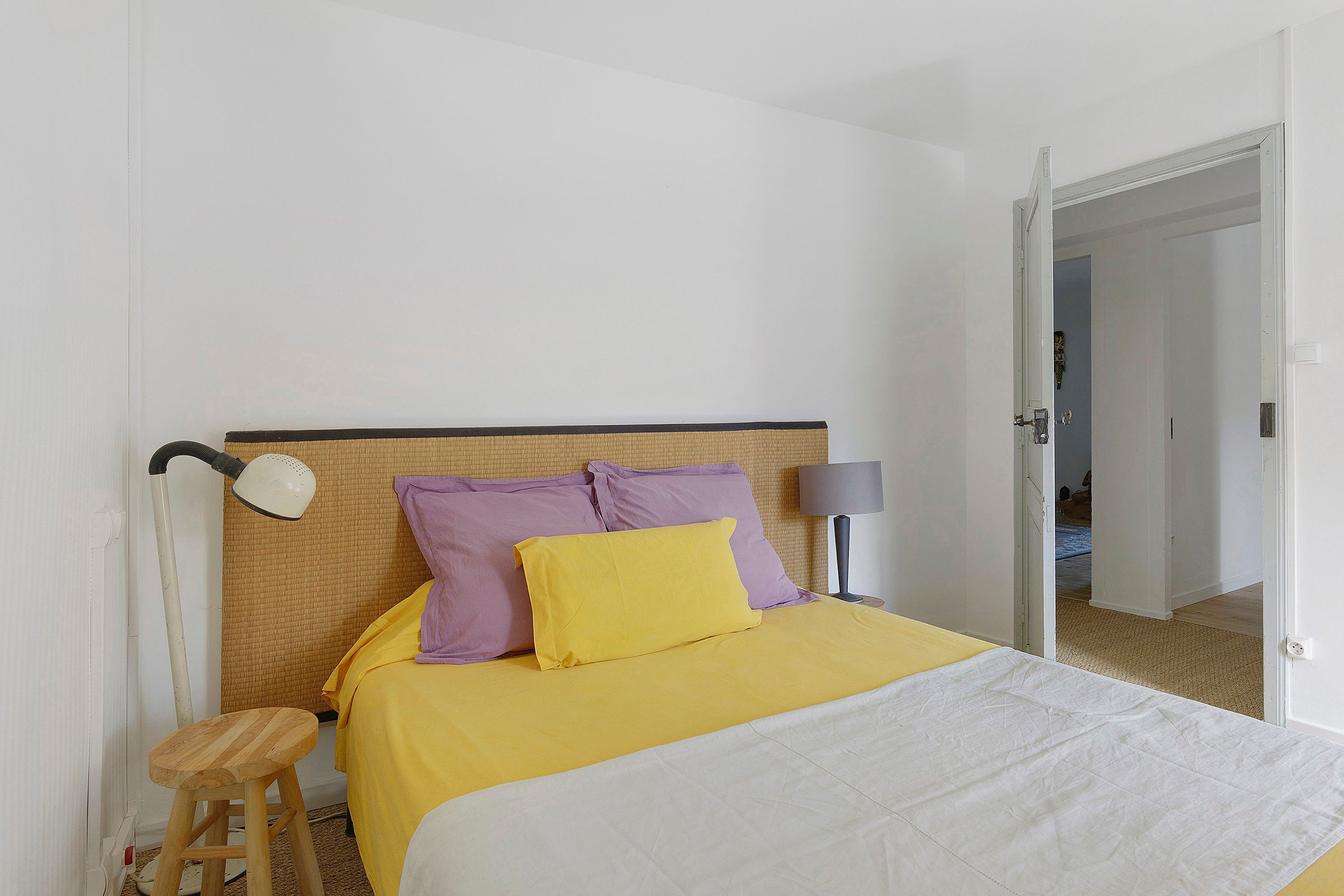 Une chambre à coucher avec un lit, une table de chevet, une lampe et un tabouret en bois.