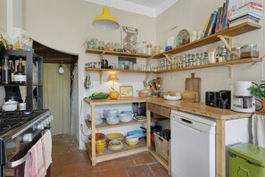 Eine kompakte Küche mit Herd, Regalen mit Gläsern, einer Kaffeemaschine und einem kleinen Kühlschrank.