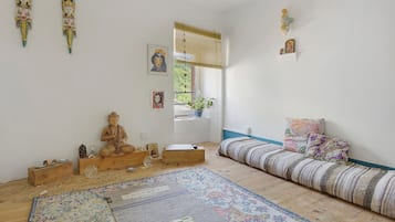 Una habitación con piso de madera, un tapete estampado, una cama con cabecera azul, un armario de madera y decoraciones en la pared, incluyendo una estatua de Buda y fotografías enmarcadas.