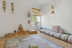 Ein Zimmer mit Holzboden, einem gemusterten Teppich, einem Bett mit blauer Kopfteil, einem Holzschrank und Wanddekorationen, darunter eine Buddha-Statue und gerahmte Bilder.