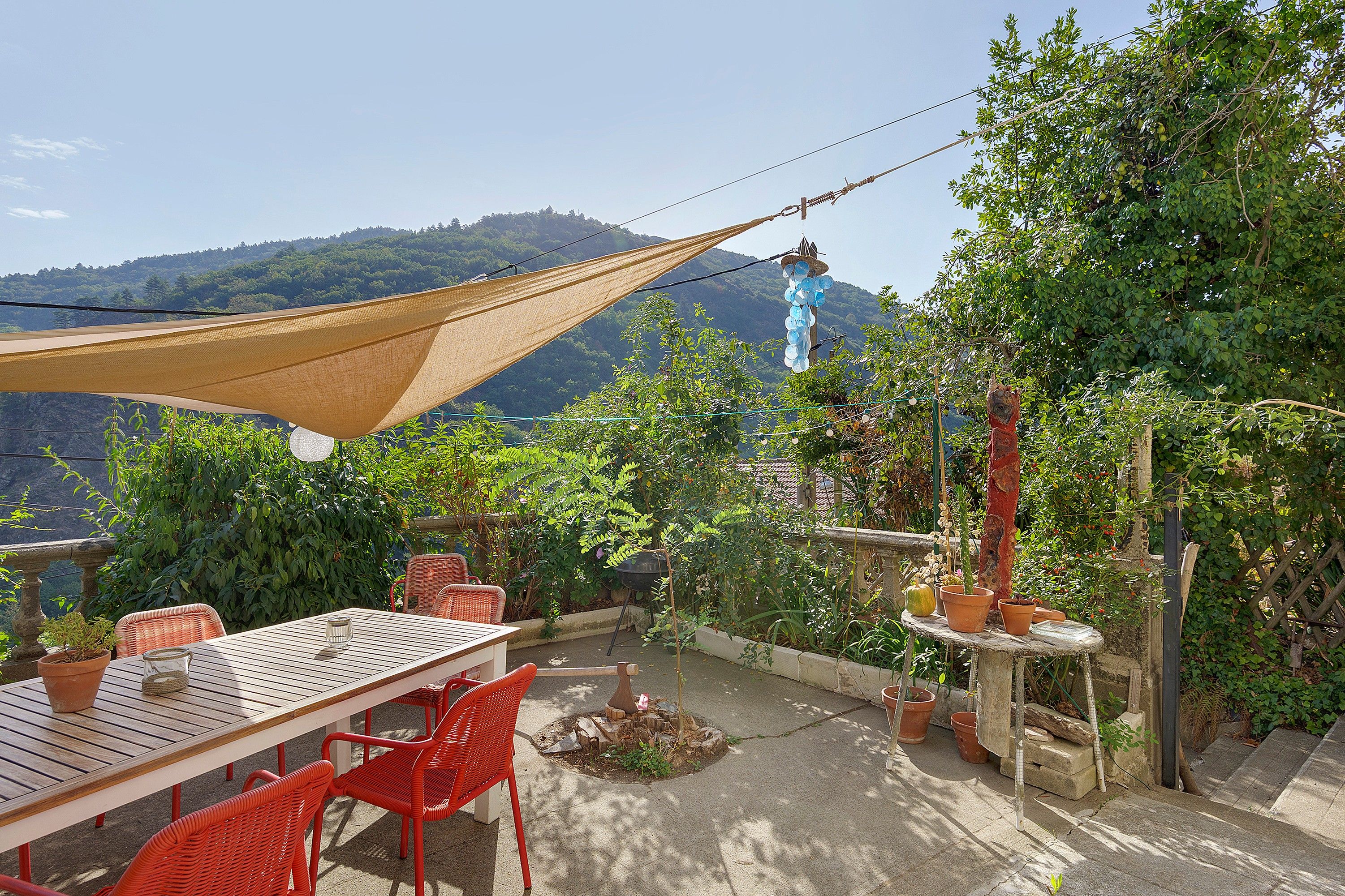 Une terrasse avec une table et des chaises, entourée de plantes en pot et agrémentée d’un hamac.