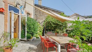 An outdoor patio with a table and chairs, surrounded by potted plants and a stone wall.
