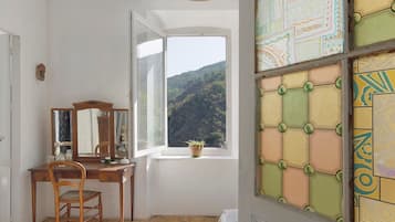 Quarto com escrivaninha de madeira, uma cadeira, janela com vista para uma montanha e um painel decorativo na parede.