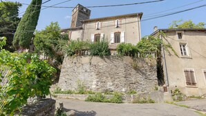A stone building with a tower, surrounded by greenery and a paved road.