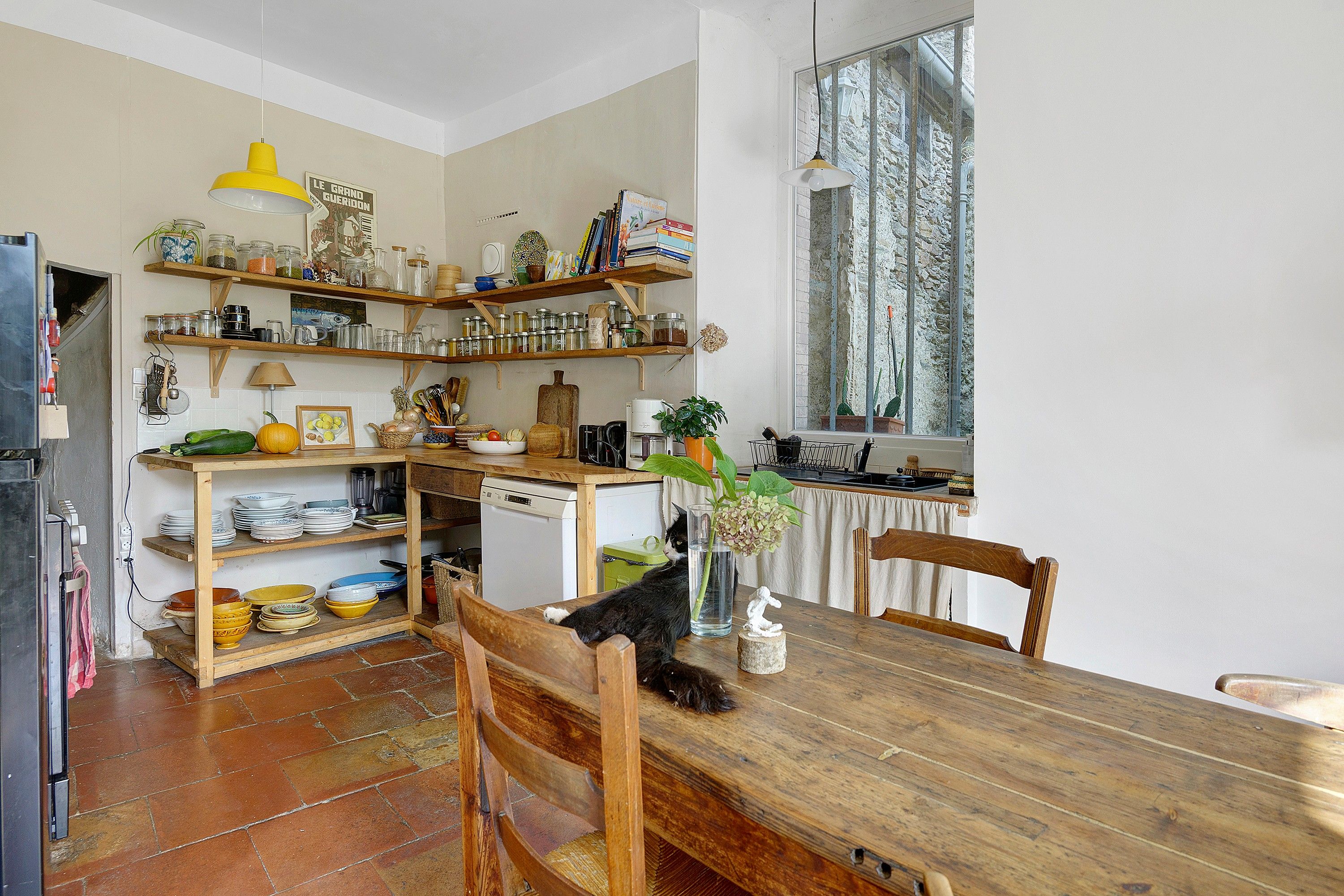 A kitchen with wooden shelves, a dining table, and a cat.