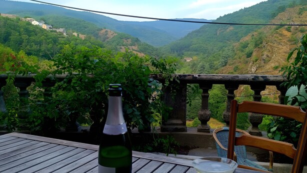 A table with a bottle of wine, two glasses, and a bowl of snacks, overlooking a mountainous landscape.