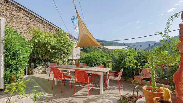 A patio with a table and chairs, surrounded by potted plants and a stone wall.