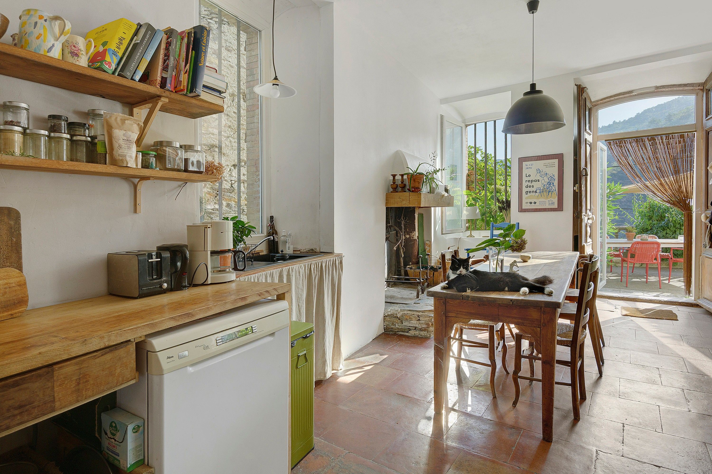 Een keuken met houten planken, een eethoek met tafel en stoelen, en uitzicht op het groen door een glazen deur.