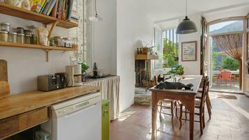 Een keuken met houten planken, een eethoek met tafel en stoelen, en uitzicht op het groen door een glazen deur.