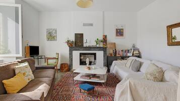 Een woonkamer met een open haard, een bank, een salontafel en een boekenkast.