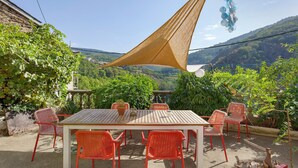 An outdoor patio with a table and chairs, surrounded by greenery and a mountainous backdrop.
