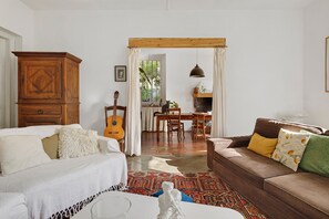 Ein gemütliches Wohnzimmer mit einer Holzkabine, einer Gitarre, einem Esstisch mit St ühlen und einer Couch mit Kissen.