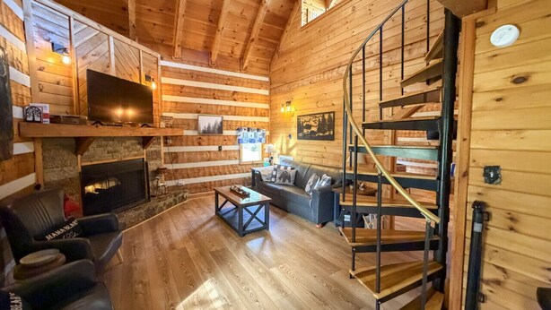 Ein gemütliches Blockhaus-Interieur mit Kamin, einer Couch, einem Couchtisch und einer Treppe.