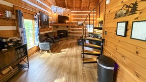 Ein gemütliches Blockhaus-Interieur mit Kamin, Holzwänden, einer Couch und einem Esstisch.